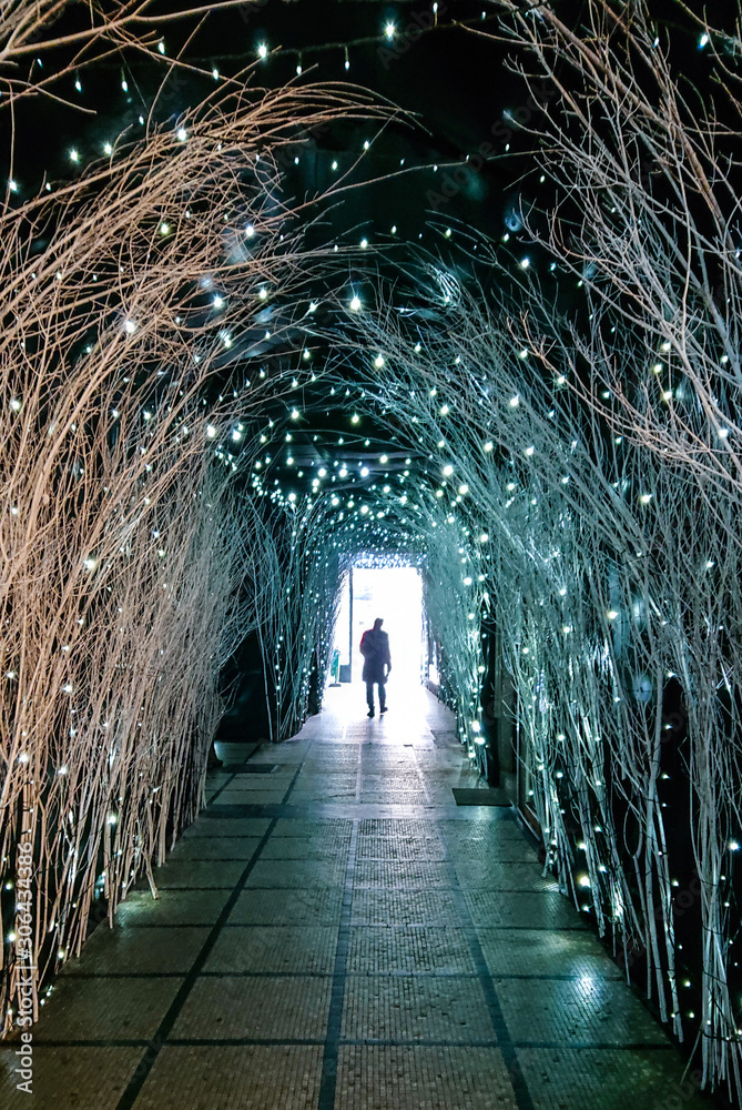VERTICAL: Unrecognizable man walks out of a passageway full of Christmas lights.