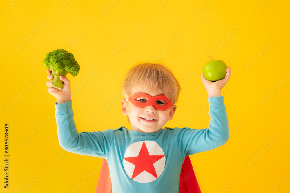 Superhero child holding broccoli and apple