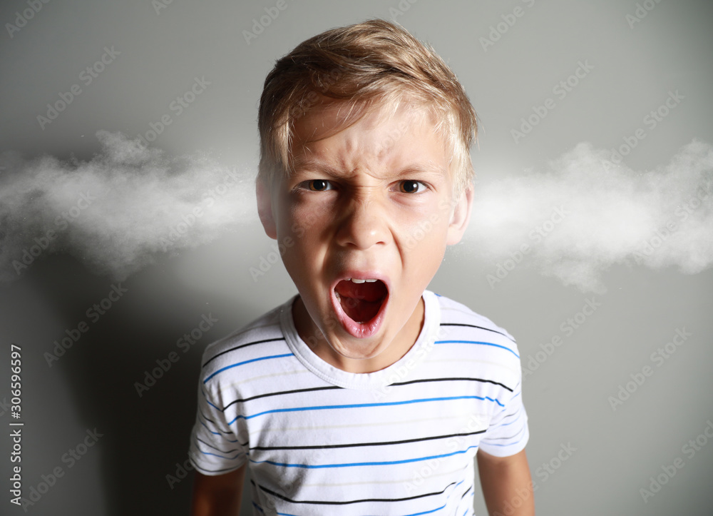 灰色背景下愤怒的小男孩从耳朵里冒出蒸汽的肖像