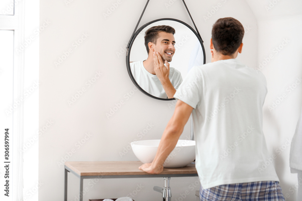 英俊的年轻人在家刮胡子后照镜子