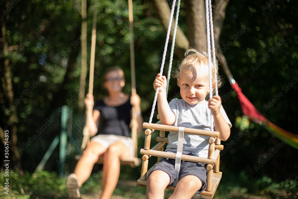Happy small child and his mother on swings outdoor in backyard