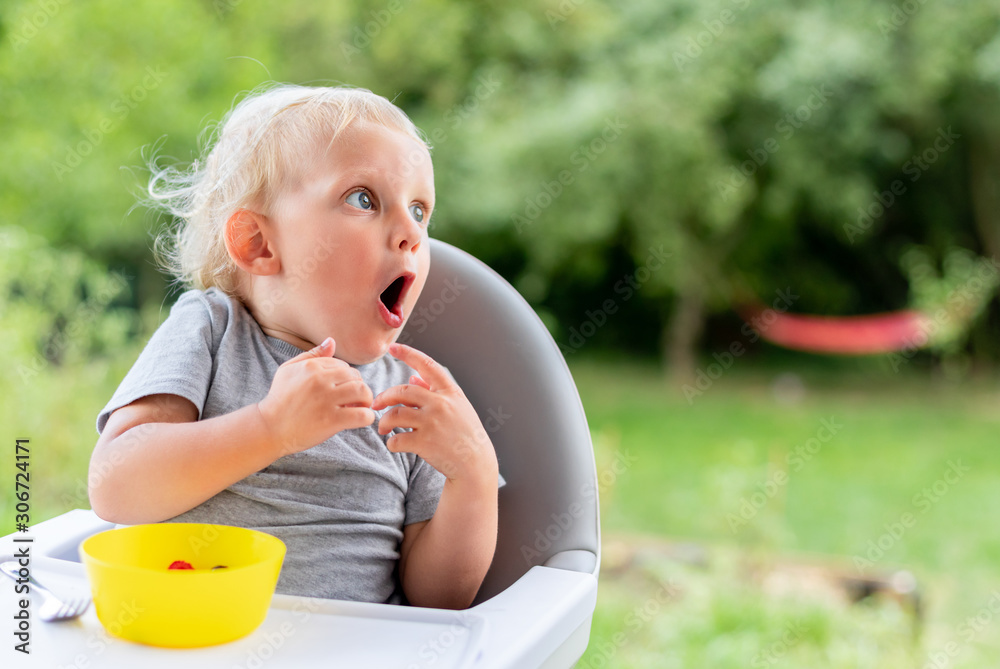 Surprised baby child looking at something while eating outdoor