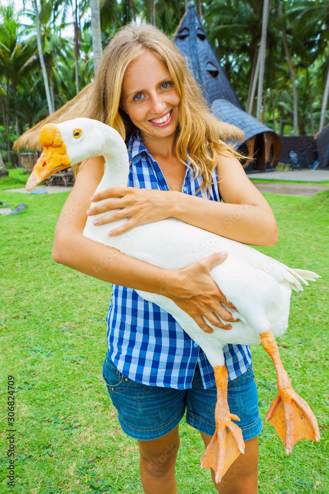 年轻快乐的女人手牵有趣的农场宠物-大白鹅。家庭夏季一日游
