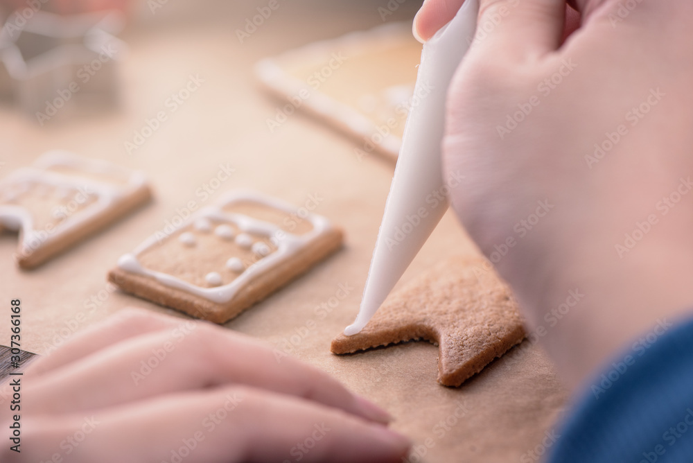 一位女士正在用木桌上的白色糖霜奶油装饰姜饼饼干屋
