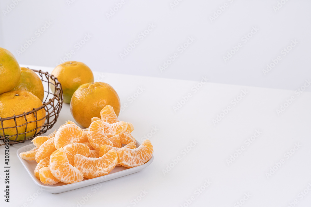 Beautiful peeled tangerines in a plate and metal basket isolated on bright white clean table in a mo