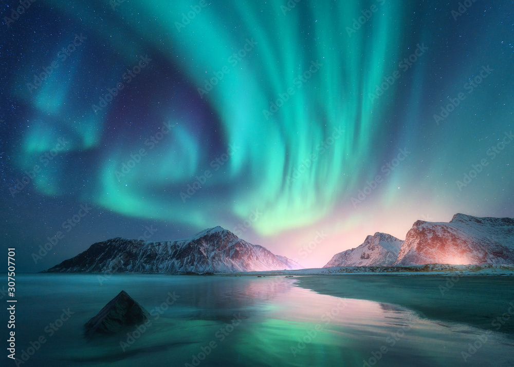 Aurora borealis over the sea and snowy mountains. Northern lights in Lofoten islands, Norway. Sky wi