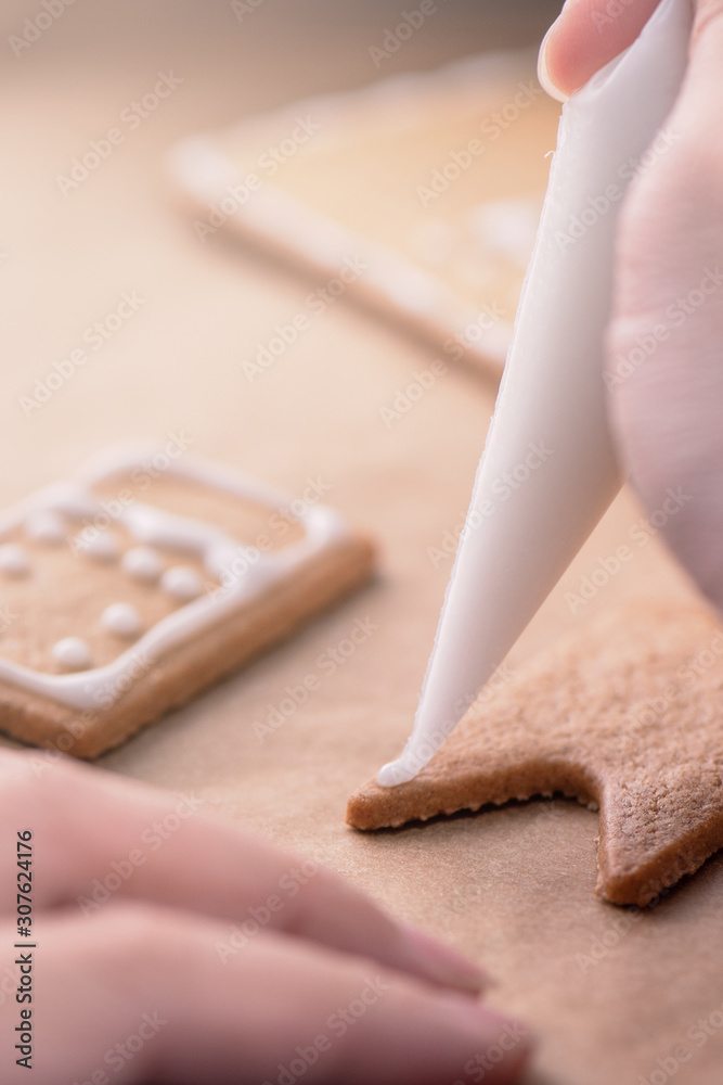 一位女士正在用木桌上的白色糖霜奶油装饰姜饼饼干屋