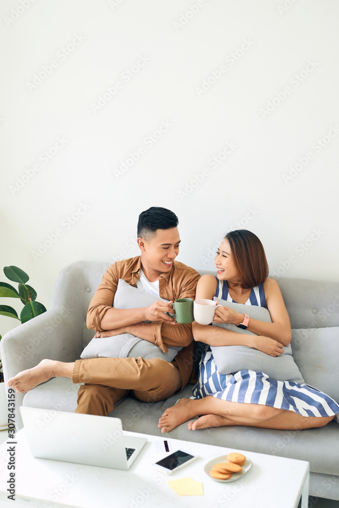 快乐的亚洲年轻情侣早上在沙发上放松，一起喝酒。