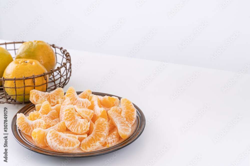 Beautiful peeled tangerines in a plate and metal basket isolated on bright white clean table in a mo