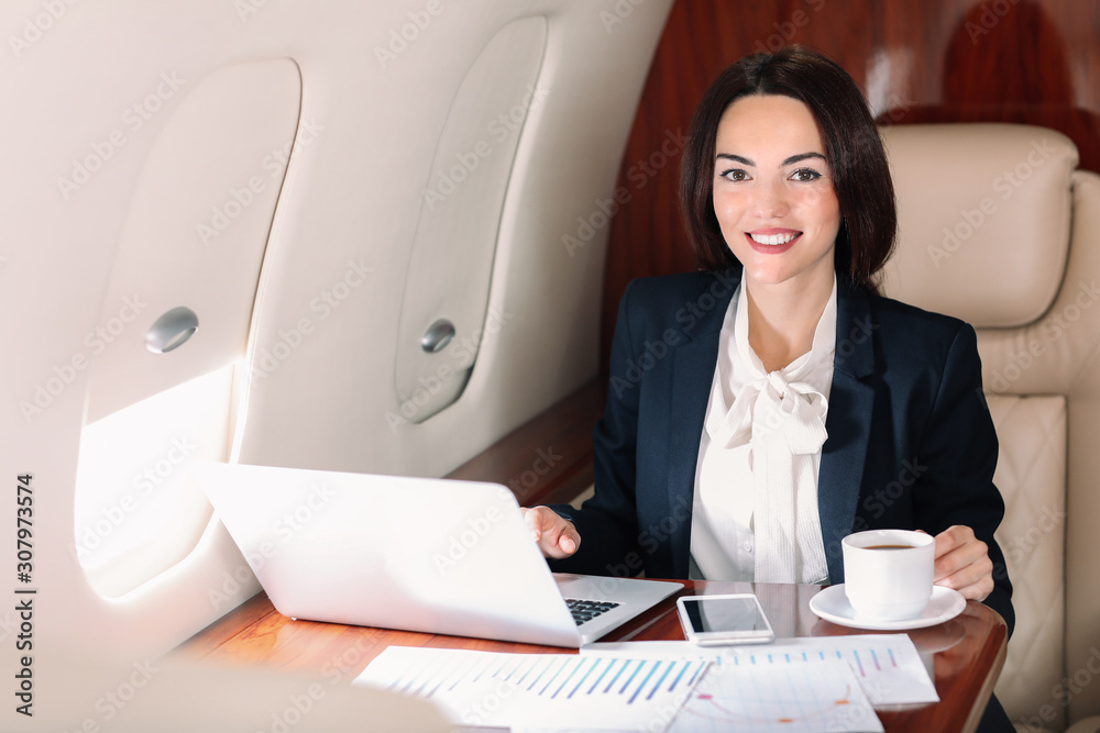 在现代私人飞机上拿着笔记本电脑喝咖啡的女商人