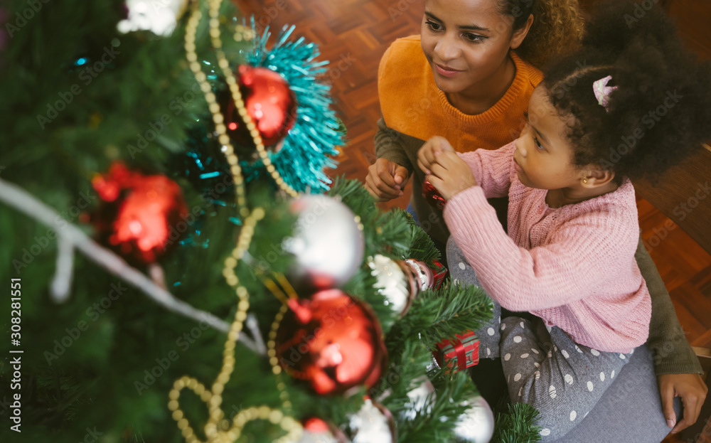 Mother and daughter african american girl decorating Christmas tree with ,arranging the christmas li