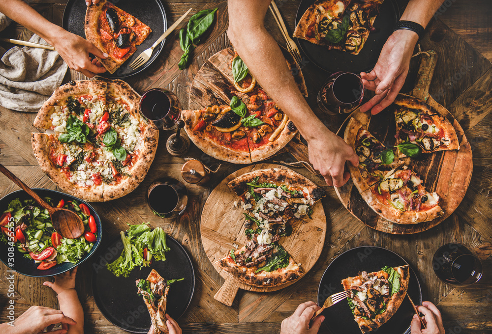 家人或朋友正在吃披萨派对晚餐。人们在吃不同种类的意大利圆周率