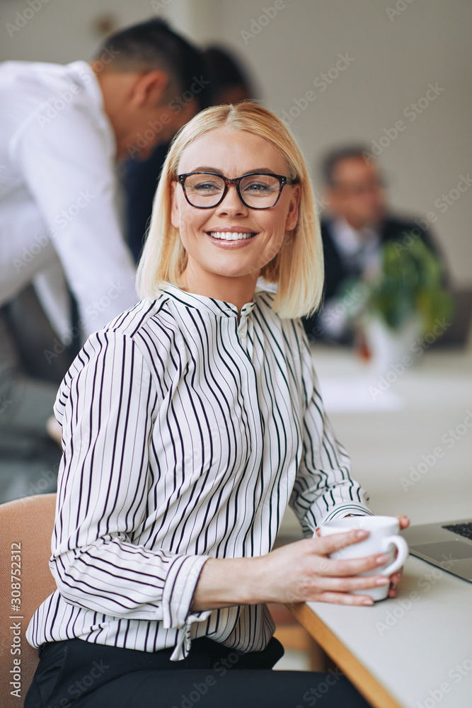 微笑的年轻女商人在办公室喝咖啡