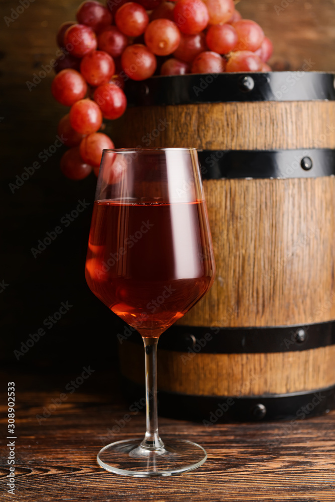 Glass of tasty wine with barrel on wooden table