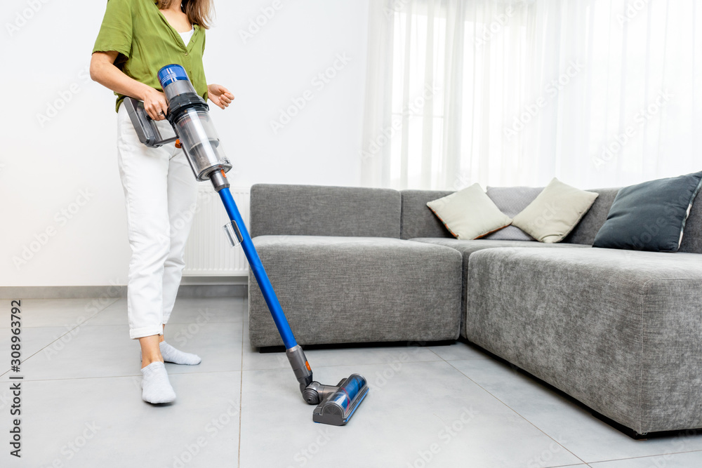 女性在现代白色客厅用无绳吸尘器清洁地板。easy c的概念