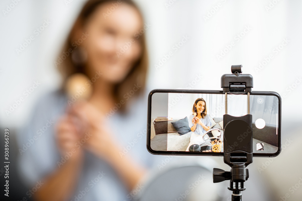 Young woman recording on a smart phone her vlog about cosmetics, showing and demonstrating makeup, c