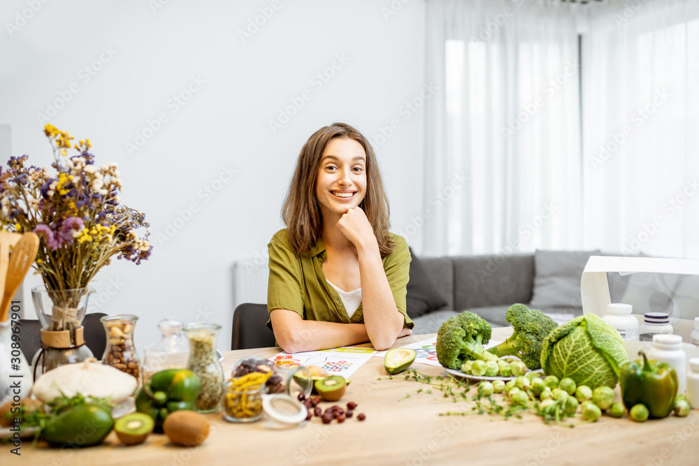 Portrait of a young cheerful woman with lots of healthy green food on the table. Concept of vegetari