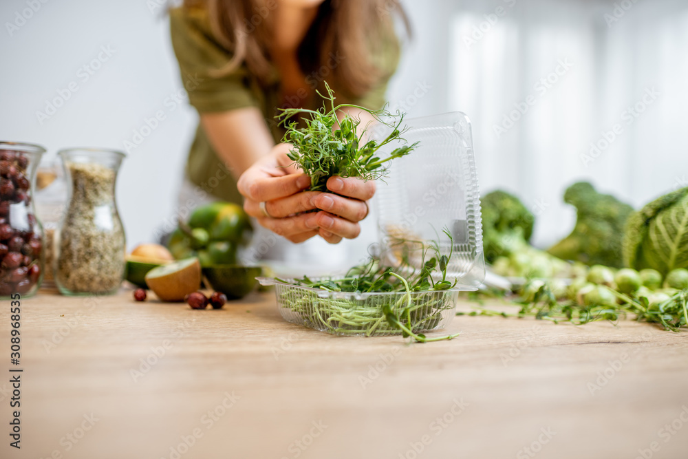 Woman holding pea seedlings with lots of healthy green food on the table. Concept of vegetarianism a