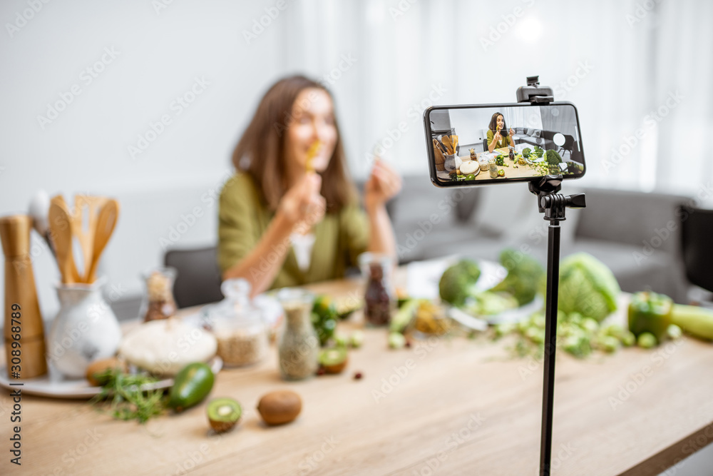 一位年轻女士在智能手机上录制了她关于健康饮食的视频日志。坐在桌子旁。
