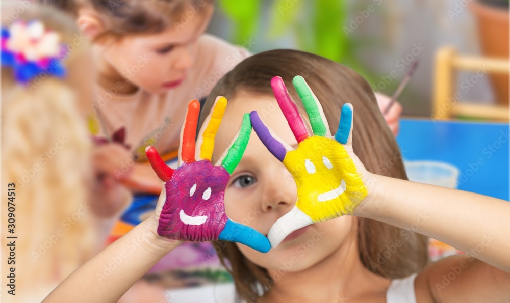 Little girl with colorful painted hands on class background