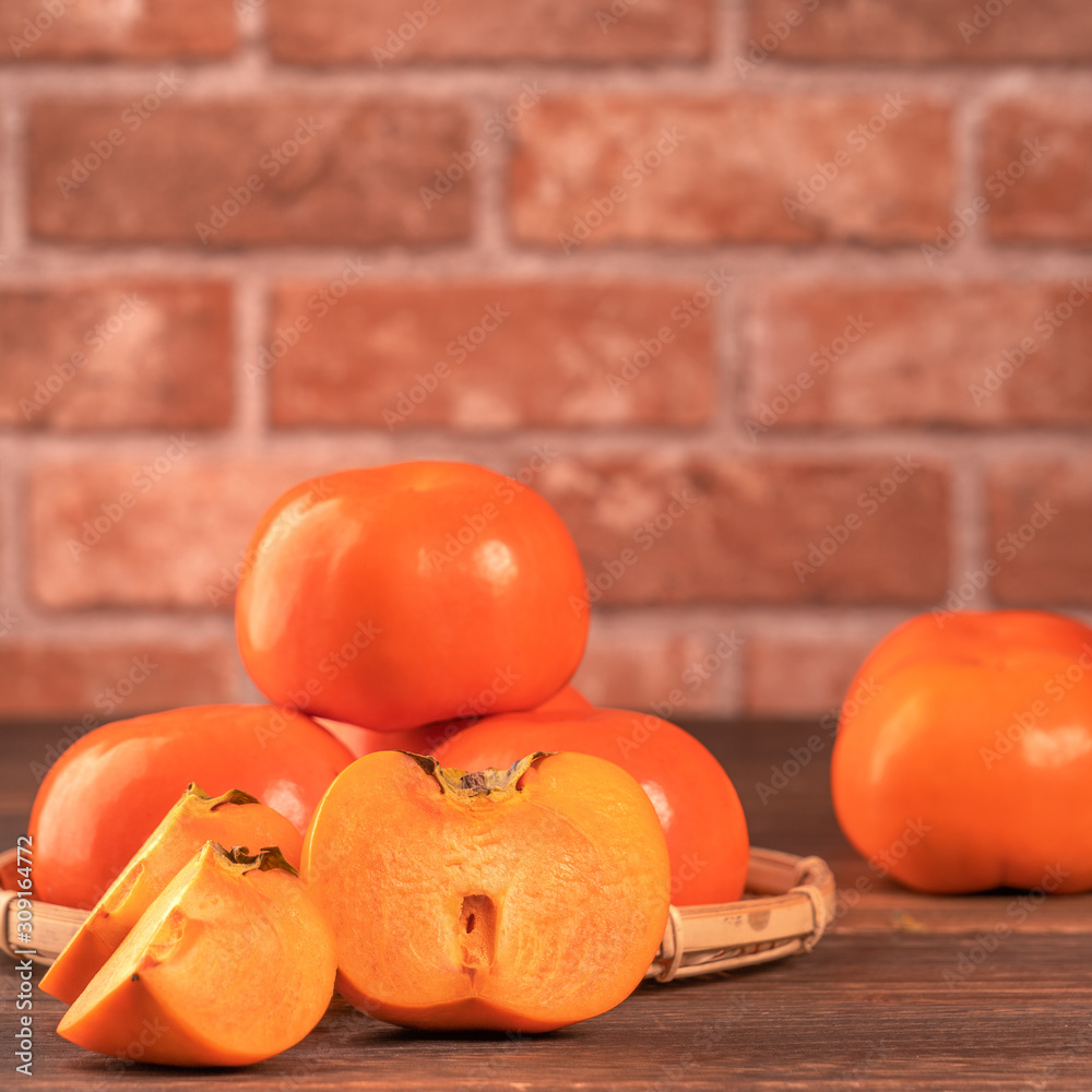 竹篮子里的甜柿子切片，放在深色木桌子上，红砖墙背景gr