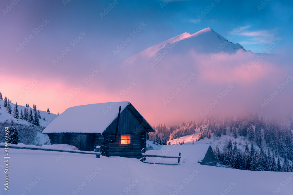 雪山中木屋的奇妙冬季景观。雾蒙蒙的阳光下高耸的山峰