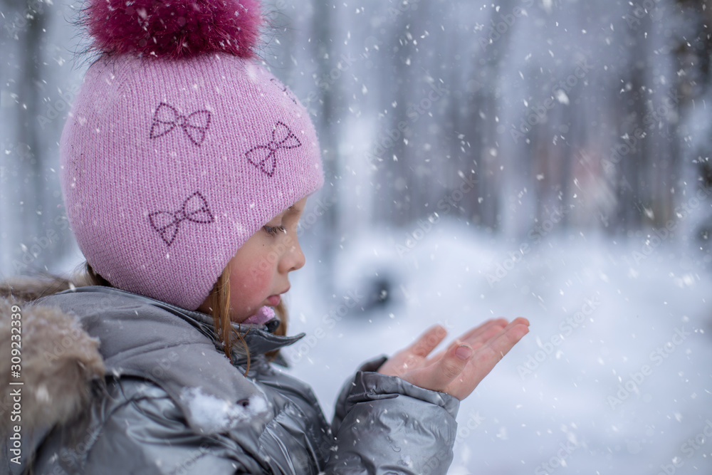 冬天，一个穿着银色夹克、戴着绒球帽的小女孩手里拿着雪花。