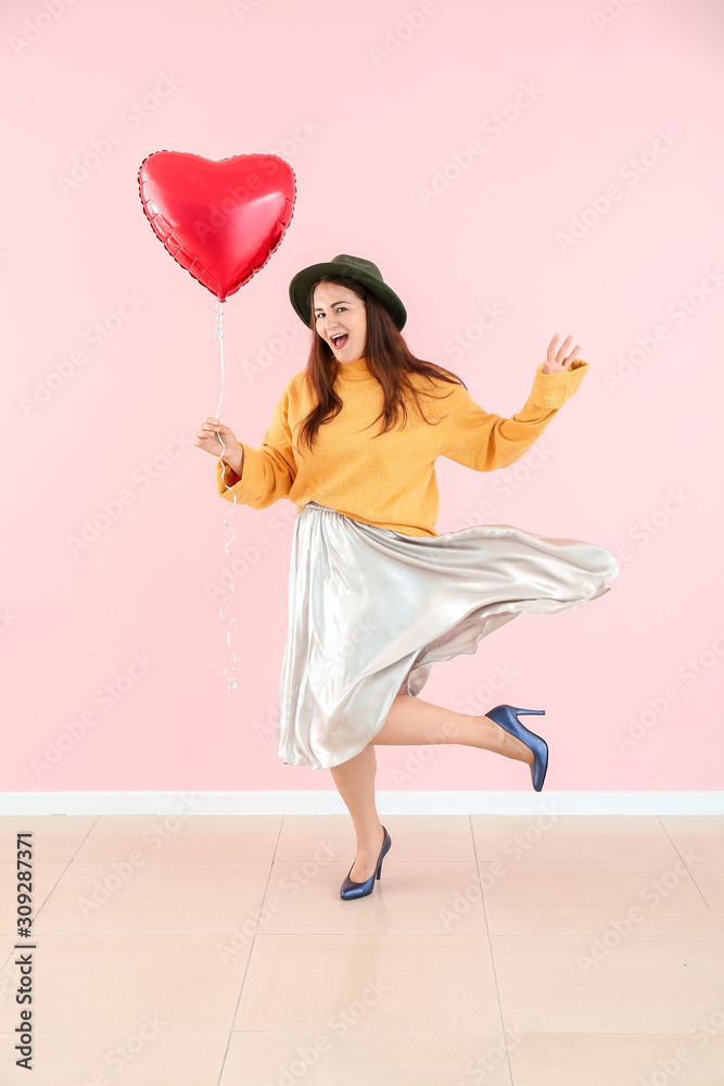 Beautiful young woman with heart-shaped balloon near color wall