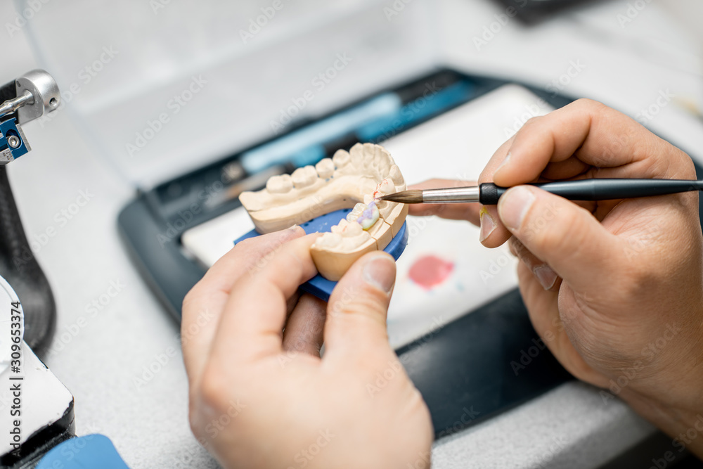 牙科技术人员在实验室用画笔为假牙上色，特写。Co