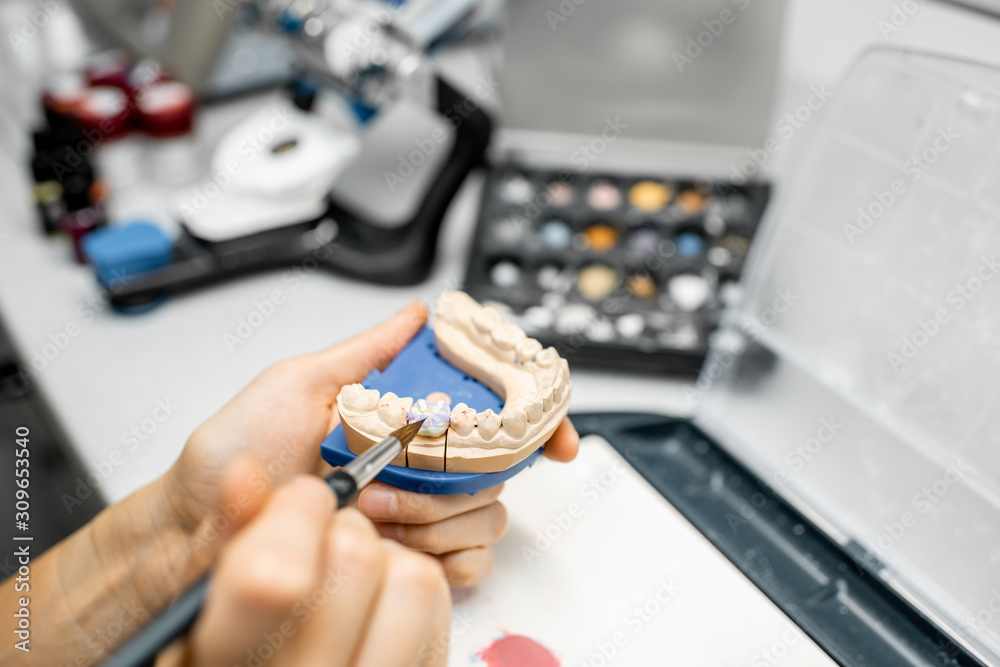 Dental technician coloring dental prosthesis with a paint brush at the laboratory, close-up view. Co