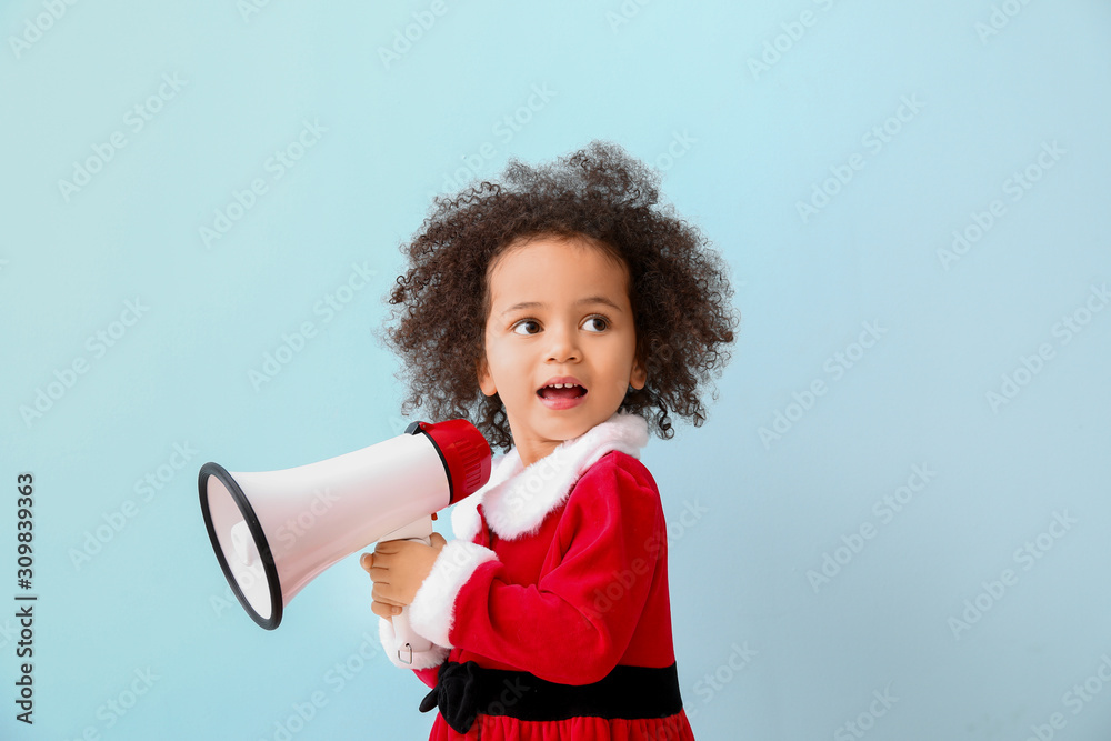 Little African-American girl in Santa costume and with megaphone on color background