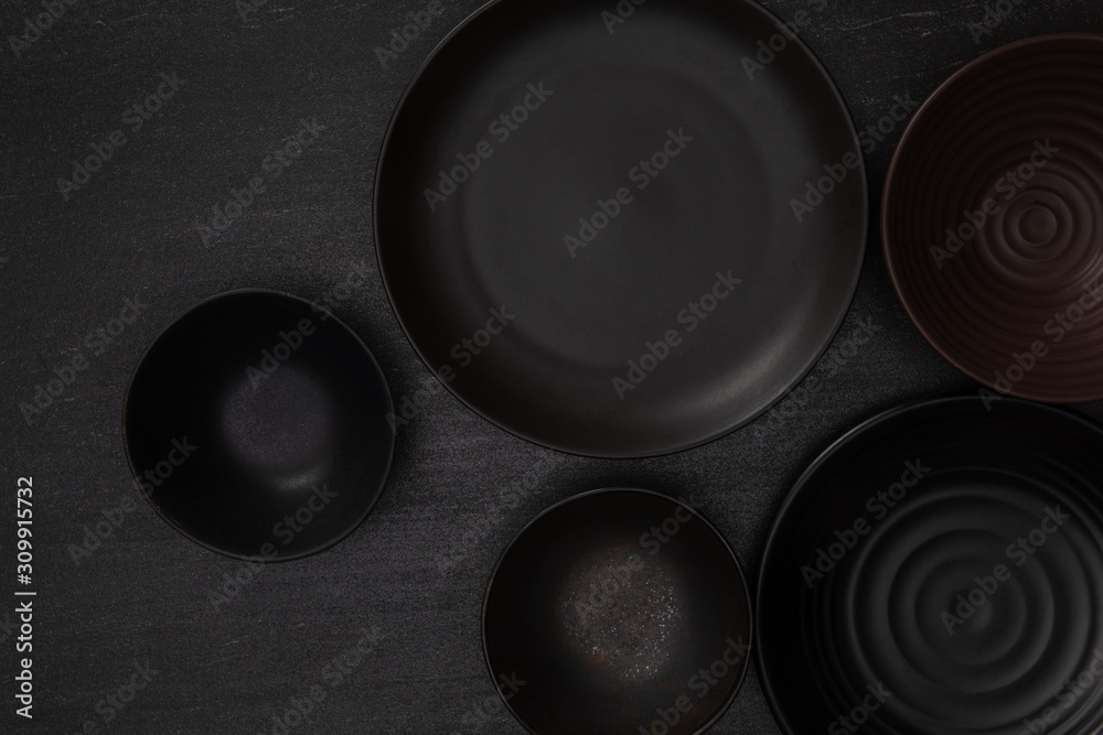 Group of empty blank black ceramic round bowls and plates on black stone blackground, Top view of tr