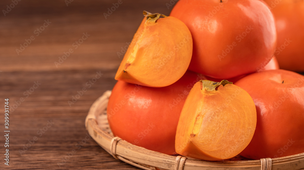 Fresh beautiful sliced sweet persimmon kaki on dark wooden table with red brick wall background, Chi