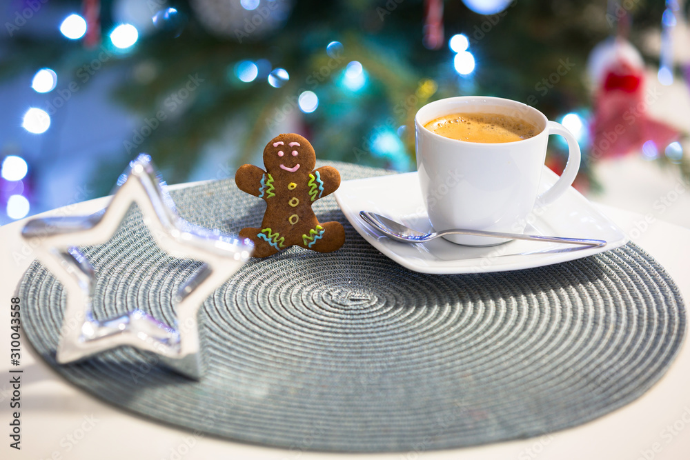 姜饼饼干人在一杯热咖啡旁，背景是圣诞树的灯光