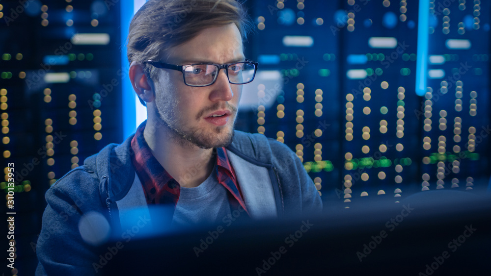 Portrait of a Smart Focused Young Man Wearing Glasses Сoncentrated on a Desktop Computer. In the Bac