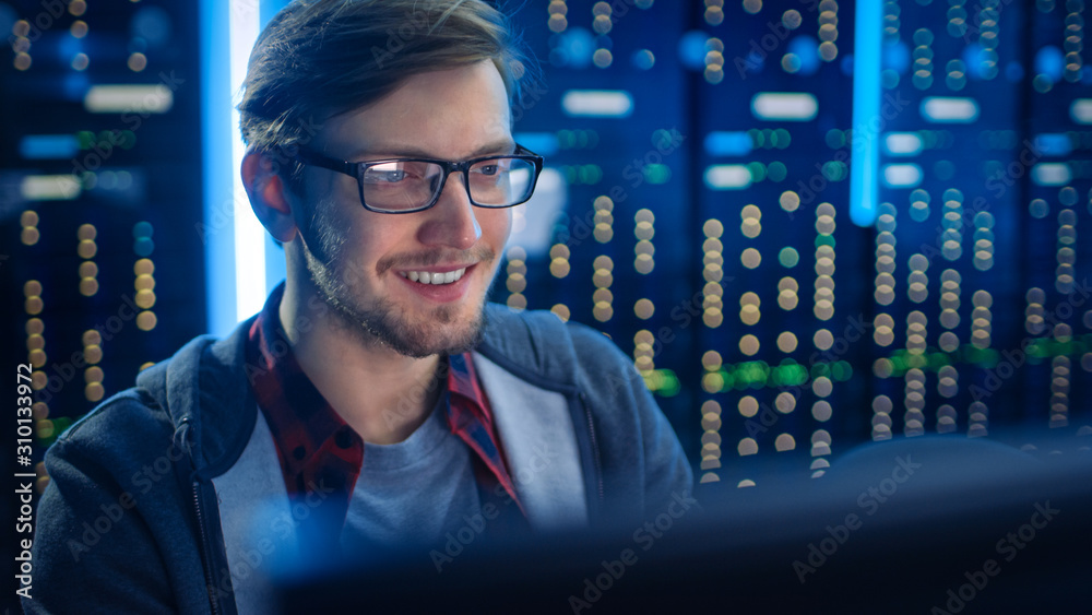 聪明微笑的年轻人戴着眼镜在台式电脑上工作的肖像。背景