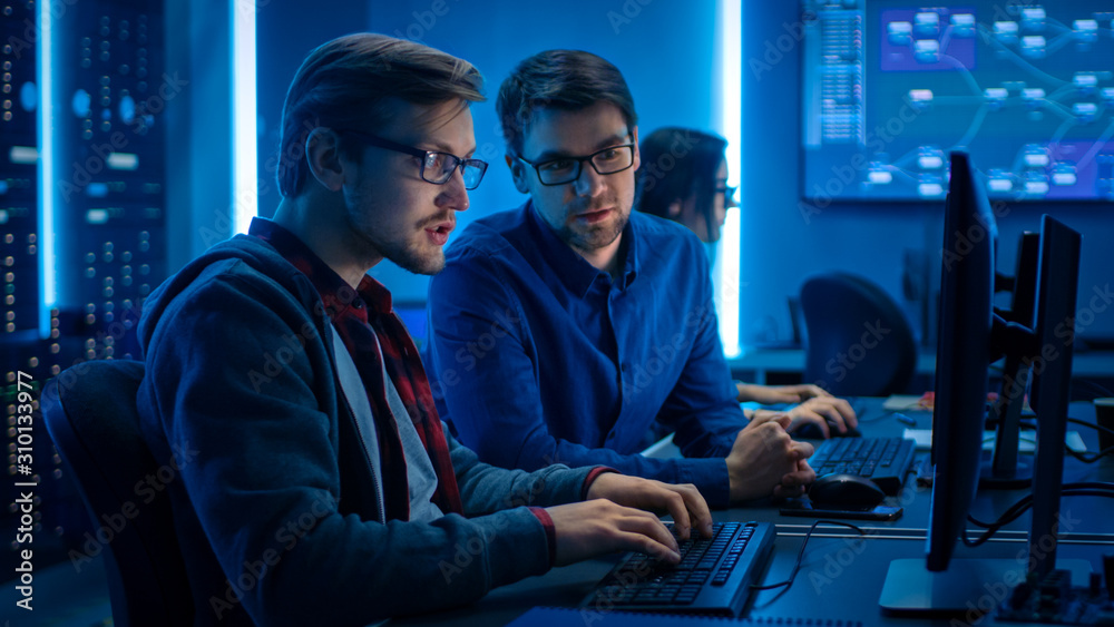 两位专业IT程序员讨论桌面电脑显示器上的技术数据显示。工作D