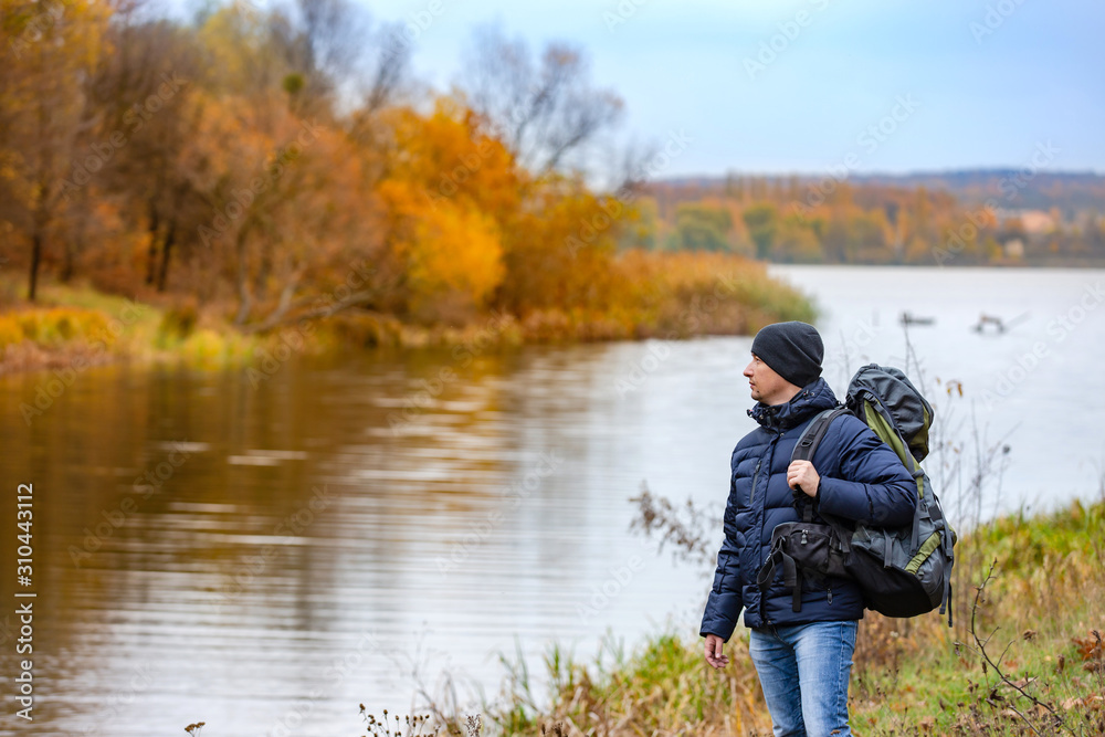 秋高气爽，背着背包的年轻人站在碧水的河岸上