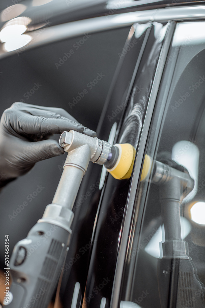 Car service worker polishing vehicle body with special wax from scratches, close-up. Professional ca