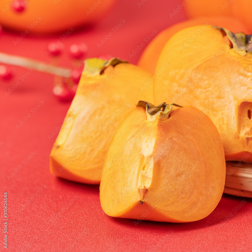Fresh beautiful sliced sweet persimmon kaki isolated on red table background and bamboo sieve, Chine