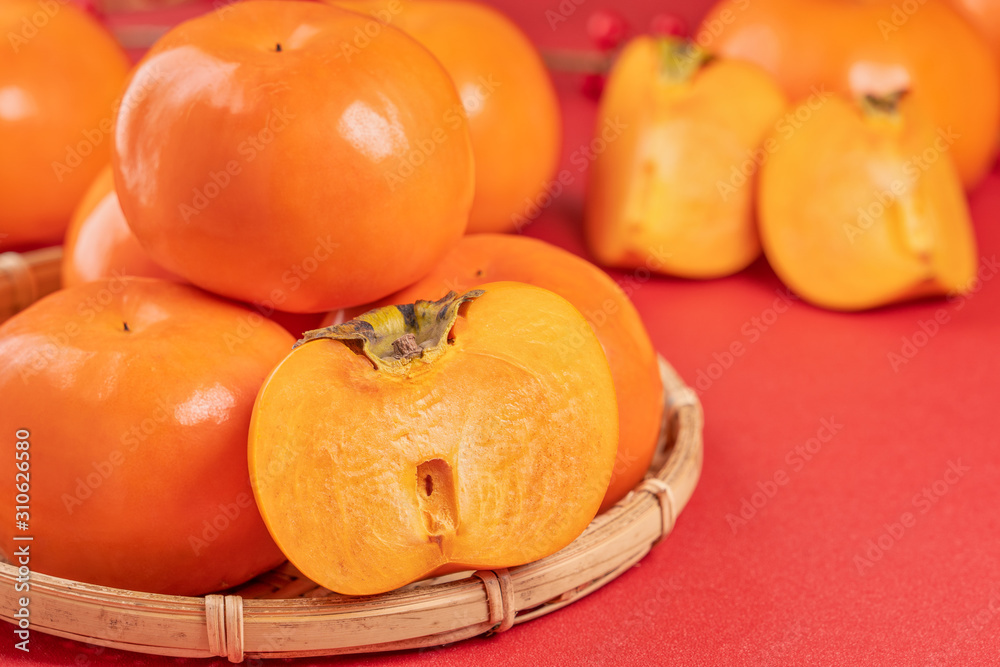 Fresh beautiful sliced sweet persimmon kaki isolated on red table background and bamboo sieve, Chine