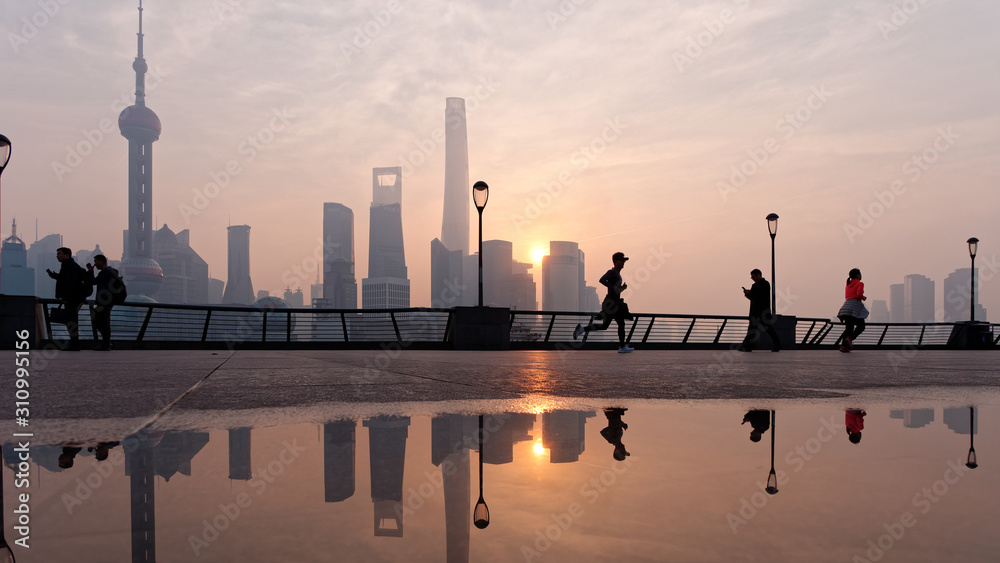 剪影晨跑者在著名的外滩区奔跑，以日出的上海为背景。
