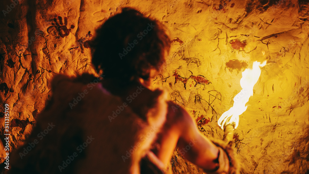 披着兽皮的原始洞穴人夜晚站在洞穴里，手持火把，看着火焰