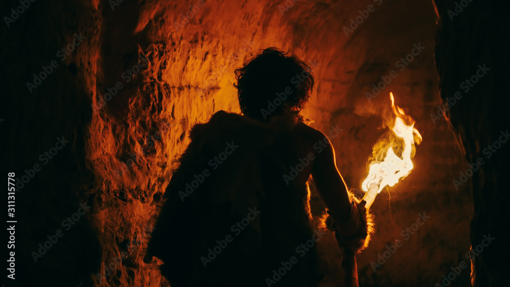 穿着兽皮的原始洞穴人晚上拿着火炬，带着火焰探索洞穴