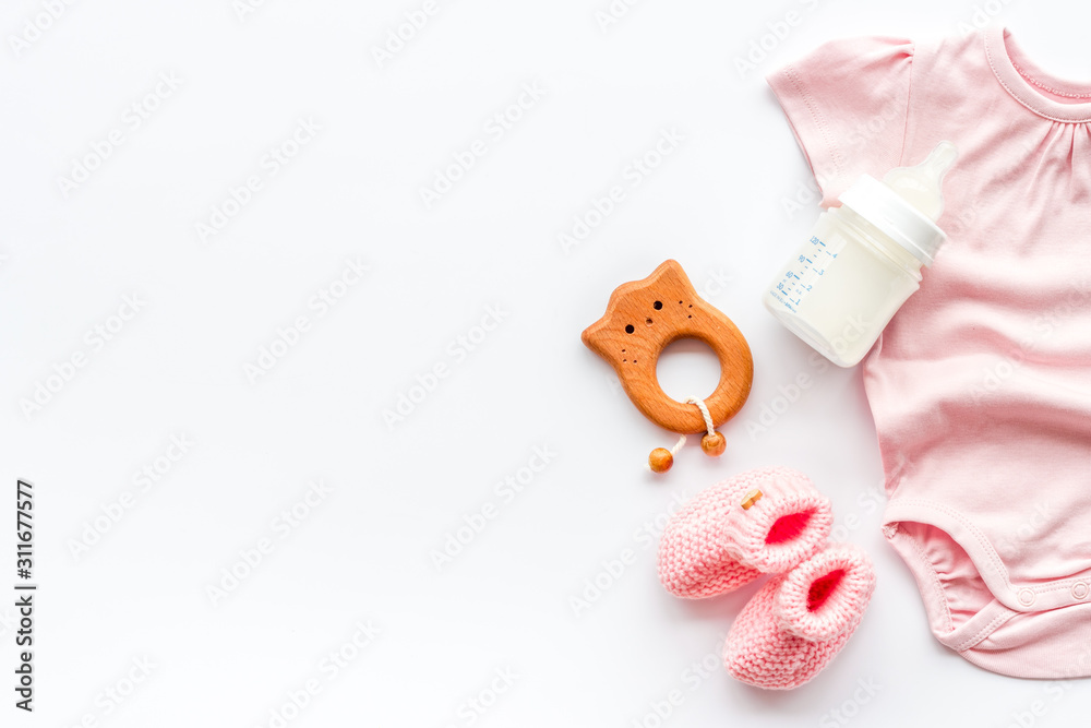 Newborn girl set - clothes as bodysuit, booties, toys - on white table top-down frame copy space