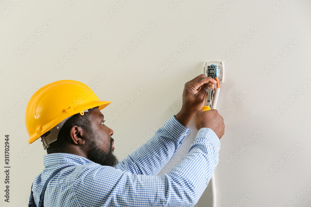 African-American electrician installing switch in room