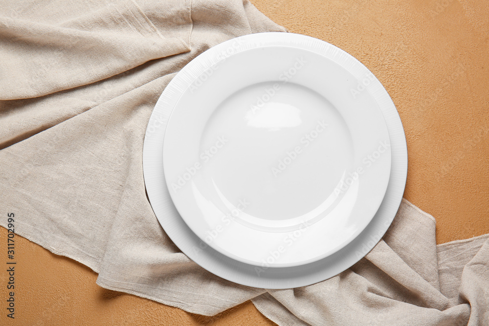 Empty plates and napkin on color background