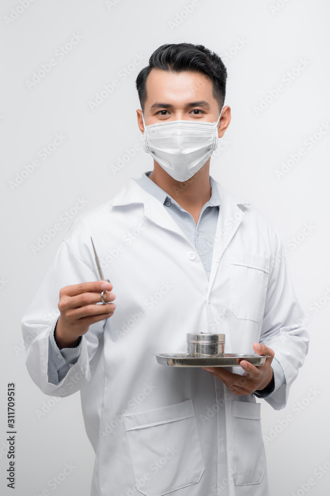 一个穿着医用外套的英俊年轻护士在托盘工具中拿着剪刀