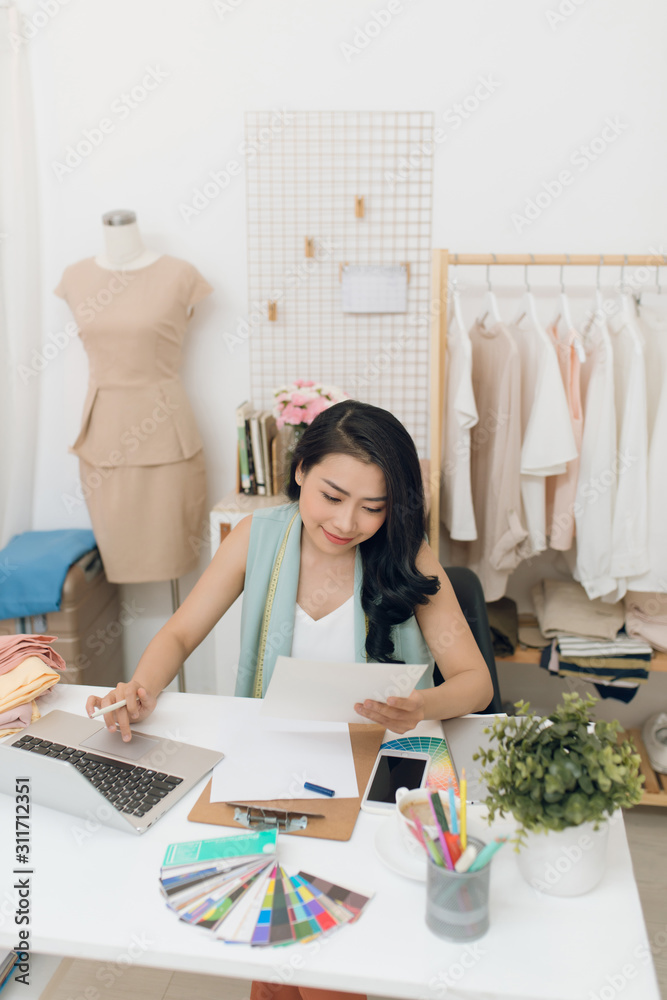 时装设计师在工作。快乐的年轻亚洲女性坐在时尚的工作场所画画