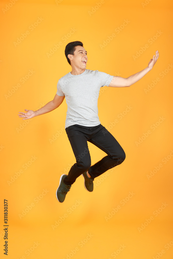活力四射、快乐的亚洲年轻人穿着休闲服跳跃，在橙色背景下拍摄隔离